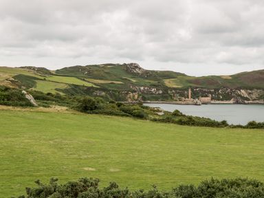 A green grassy field with hills and a body of water with buildings in the background at Porthwen Lodge in Bull Bay near Cemaes Bay