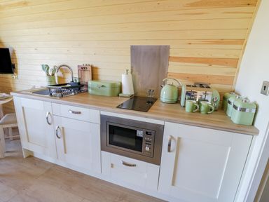 A kitchen counter with white cabinets and wooden countertop with a microwave sink kettle and toaster in Tamina Hillhampton Great Witley