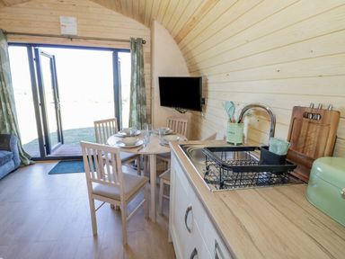 A kitchen and dining area with a round table set for four near open glass doors at Tamina in Hillhampton Great Witley