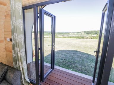 An open glass door leading to a grassy outdoor area with hills in the distance at Tamina in Hillhampton Great Witley