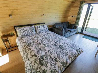 A bedroom with a bed sofa side tables and glass doors leading outside at Tamina in Hillhampton Great Witley