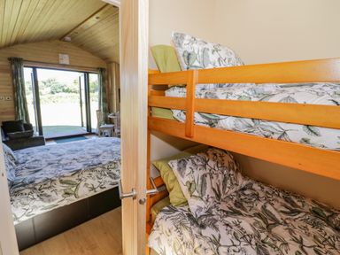 A bedroom with bunk beds and a double bed with floral bedding next to a room with a sofa and a table at Tamina in Hillhampton Great Witley
