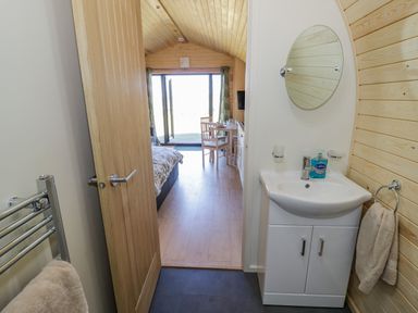A bathroom with a sink and mirror looking into a room with a bed table and chairs at Tamina in Hillhampton Great Witley
