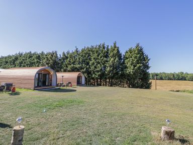 Two wooden pod cabins on a grassy field with trees in the background at Tamina in Hillhampton Great Witley