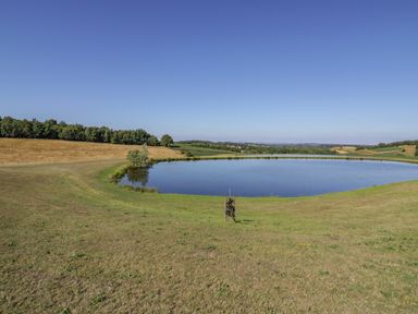 A pond surrounded by grass and fields with trees and hills in the background at Tamina Hillhampton Great Witley