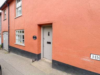 An exterior view of a building with an orange wall a gray door a window and a street sign at Forge House in Cley Next The Sea