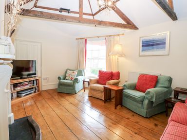 A sitting room with armchairs cushions wooden floor and exposed beams at Forge House in Cley Next The Sea