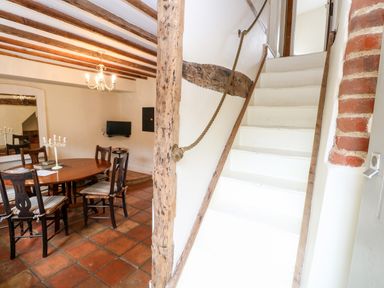 A dining area with wooden table and chairs next to white stairs with rope handrail at Forge House in Cley Next The Sea