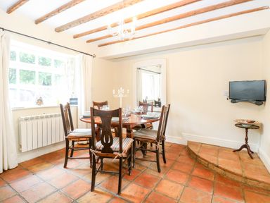 A dining room with a round wooden table and six chairs under exposed wooden beams at Forge House in Cley Next The Sea