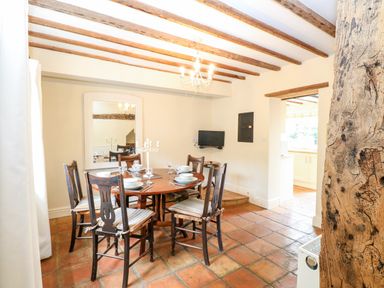 A dining room with wooden chairs and table set for dinner under ceiling beams at Forge House in Cley Next The Sea