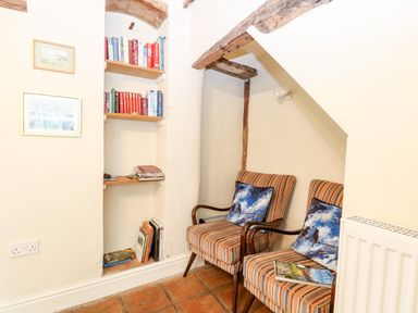 A corner with two striped chairs with blue pillows next to a built-in bookshelf with books at Forge House in Cley Next The Sea
