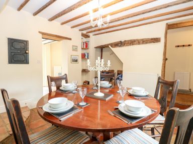 A dining room with a round wooden table set for six with white plates bowls and glasses at Forge House in Cley Next The Sea