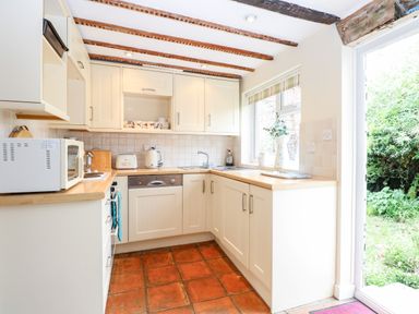 A kitchen with white cabinets wooden countertops and terracotta floor tiles at Forge House in Cley Next The Sea