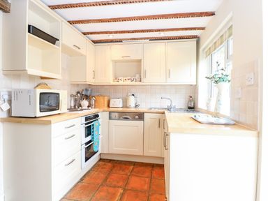 A kitchen with white cabinets wooden countertops a microwave oven a stove a toaster and a sink at Forge House in Cley Next The Sea
