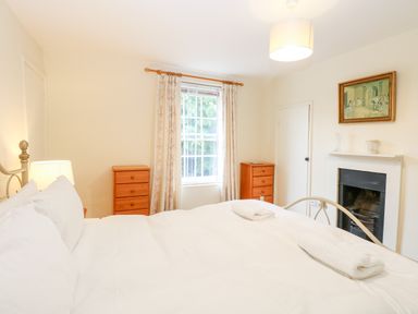 A bedroom with a bed near two wooden dressers and a window with curtains at Forge House in Cley Next The Sea