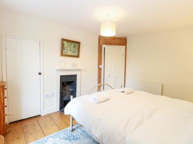 A bedroom with a bed and white bedding a wooden floor a fireplace and a framed picture above the fireplace at Forge House in Cley Next The Sea