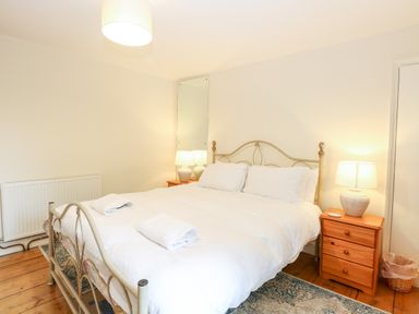 A bedroom with a metal bed frame white bedding wooden nightstands lamps and a mirror at Forge House in Cley Next The Sea