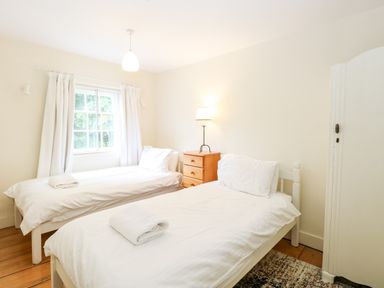 A bedroom with two single beds white bedding a wooden chest of drawers and a window with curtains at Forge House in Cley Next The Sea