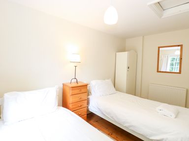 A bedroom with two single beds a wooden bedside table with a lamp a white wardrobe and a mirror on the wall at Forge House in Cley Next The Sea