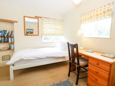 A bedroom with a single bed desk chair lamp bookshelf and window blinds with stars at Forge House in Cley Next The Sea