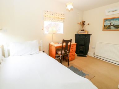 A bedroom with a single bed desk chair lamp and fireplace at Forge House in Cley Next The Sea