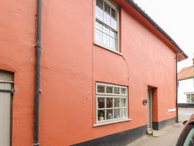 The exterior of a two story orange building with two windows a door black drainpipes and a street sign that says High Street at Forge House in Cley Next The Sea