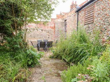 A garden with plants and outdoor chairs and table near stone walls at Forge House in Cley Next The Sea