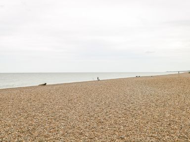A pebble beach with a few people fishing near the water and a small boat by the shore at Forge House in Cley Next The Sea
