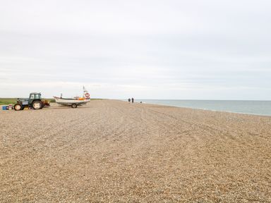 A pebble beach with a tractor and boat trailer and two people walking near the sea at Forge House in Cley Next The Sea
