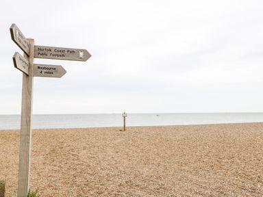 A pebble beach with a wooden signpost showing directions to Norfolk Coast Path Weybourne and Cley Next The Sea