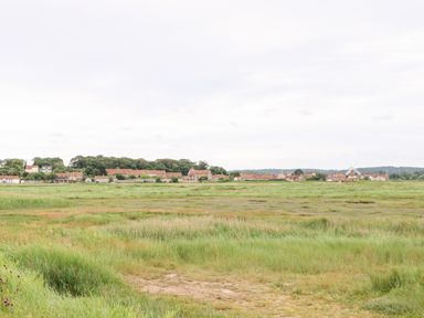 A large grassy field with houses and a windmill in the background at Forge House in Cley Next The Sea