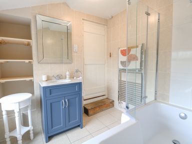 A bathroom with a blue vanity unit sink a mirror a wooden step a white stool and a towel on a radiator at Forge House in Cley Next The Sea