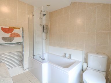 A bathroom with a bathtub and shower, a toilet, tiled walls, and a towel on a metal rack at Forge House in Cley Next The Sea