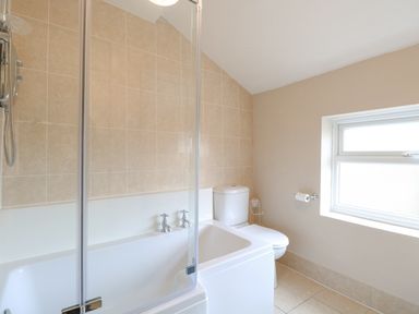 A bathroom with a bathtub shower and toilet near a window at Forge House in Cley Next The Sea