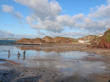 A beach with rocks people walking and houses on cliffs at Goody in Hope Cove