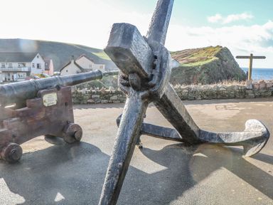 An outdoor area with a large metal anchor and a cannon near houses and a hill by the sea at Goody in Hope Cove