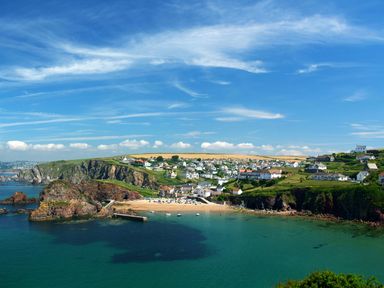 A coastal village with houses on hills and a small sandy beach with boats in the water at Goody in Hope Cove