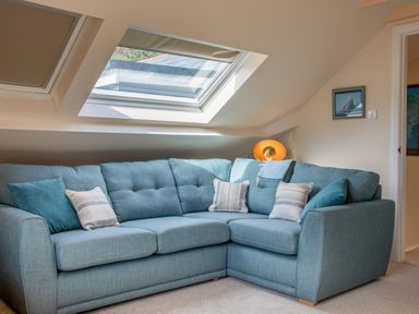 A blue sectional sofa with cushions under a skylight window and a lamp on the side at Goody in Hope Cove