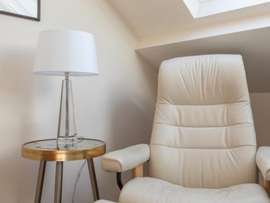 A beige armchair next to a round side table with a lamp in a room at Goody Hope Cove