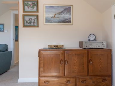 A wooden cabinet with a clock and stereo on top and three framed pictures on the wall in a living room at Goody in Hope Cove