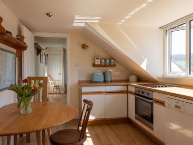 A kitchen with a wooden table and chairs a vase of flowers toaster kettle and stove at Goody in Hope Cove