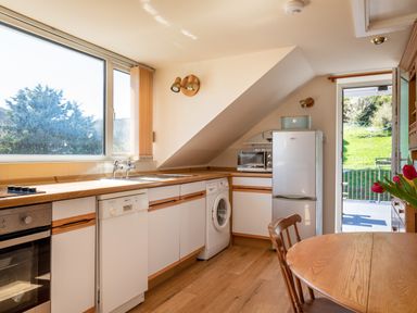 A kitchen with white appliances and wooden countertops near a window and a door opening to a garden at Goody in Hope Cove