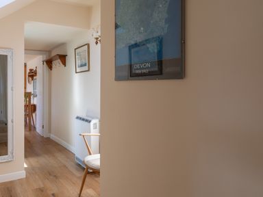 A hallway with wooden floor a chair a wall heater and framed pictures at Goody in Hope Cove
