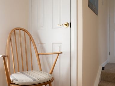 A wooden chair with a striped cushion next to a white door with a brass handle