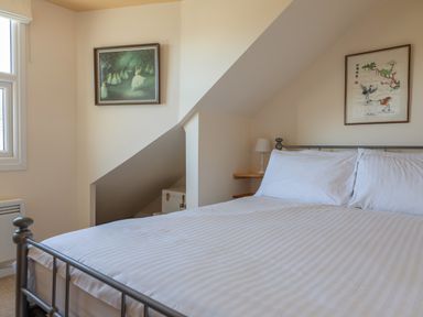 A bedroom with a metal bed frame and white bedding two framed pictures on the walls and a small lamp on a wooden shelf at Goody in Hope Cove