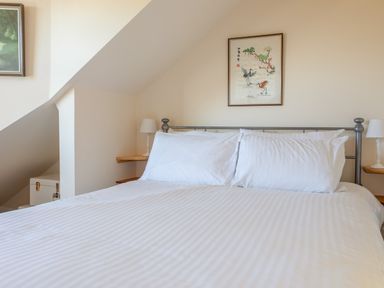 A bedroom with a white bedspread and pillows two bedside lamps and two framed pictures on the walls at Goody in Hope Cove