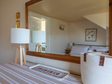 A table with a lamp and tray in front of a large wooden mirror reflecting a bedroom with a bed and framed picture at Goody in Hope Cove