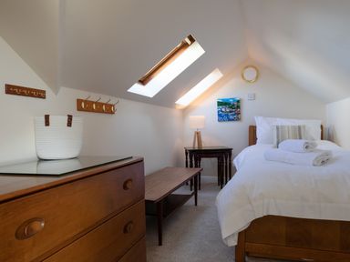 A bedroom with a single bed towels bedside tables a white basket on a dresser and coat hooks on the wall at Goody in Hope Cove