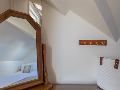 A wooden framed mirror reflecting a bed with a striped pillow and a white basket with brown handles on a surface at Goody in Hope Cove