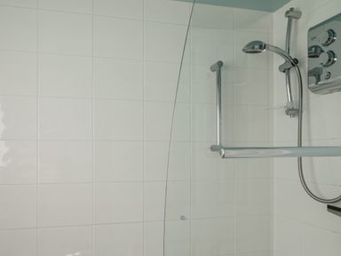 A shower area with a handheld showerhead a glass screen and white tiled walls at Goody in Hope Cove